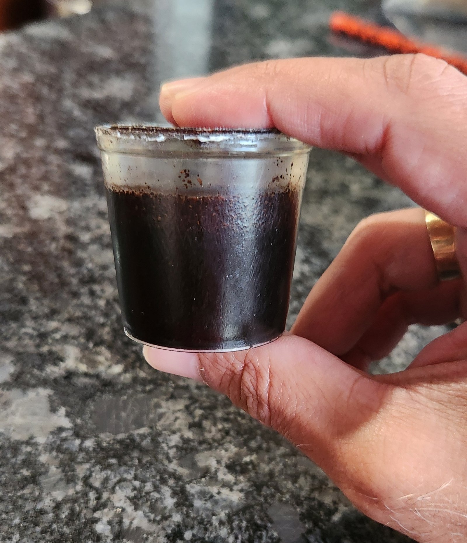 A Naturista machine pod held between two fingers, brewed coffee inside the clear pullulan cup